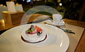 Pavlova cake with with fresh strawberries, blueberries and mint leaves on a white ceramic plate on restoran table