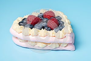 Pavlova meringue cake decorated with fresh raspberry and blueberry berries on blue background
