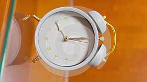 Paw of dog turns off white vintage alarm clock with large bells, standing on glass bedside table, showing 8 o'clock