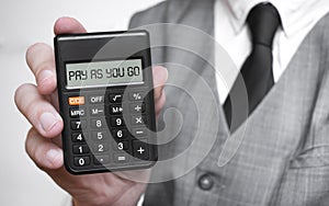 PAY AS YOU GO word text inscription on calculator in a male hand of a businessman in white shirt and blue tie, Concept of finance