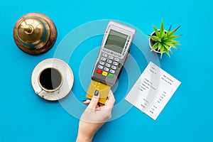 Pay the bill by payment terminal. Woman`s hand insert bank card in payment terminal near bill, service bell, coffee and