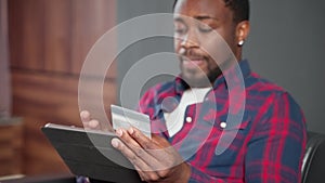 pay by card in internet service, portrait of african man entering credit card details on tablet