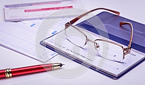 Pay with check instantly, on time. Glasses on a checkbook, red pen, financial documents on the background. Closeup, financial conc