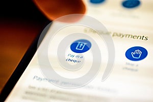 Pay in cheque button on smartphone app screen closeup with human finger pointing to it