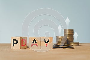 Pay day loan concept, pay day text on wooden cube block and blurred stack of coins and blurred arrow up above