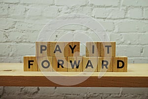 Pay It Forward alphabet letter on white brick wall and wooden shelves background