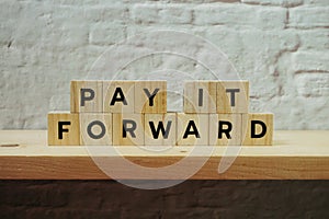 Pay It Forward alphabet letter on white brick wall and wooden shelves background