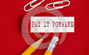 PAY IT FORWARD message written on torn red paper with pencils and clips, business