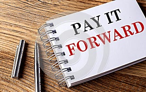 PAY IT FORWARD text on notebook with pen on wooden background