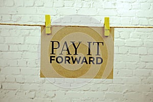 Pay it forward text on paper card hanging on the wall with Clothespins