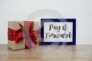 Pay it forward typography text and gift box on wooden table and white wall background