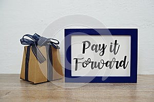 Pay it forward typography text and gift box on wooden table and white wall background
