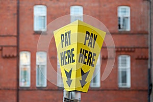 a pay here sign on top of a pay and display ticket car park machine