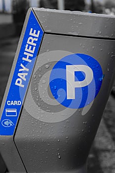 a pay here sign with water droplets sitting on a parking meter