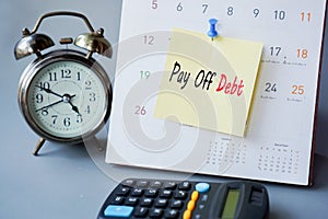 Pay off debt concept with remind note on calendar with clock and calculator on desk
