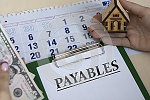 PAYABLES - word in a folder against the background of women`s hands with a house and money