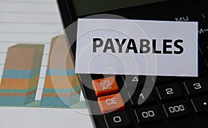 PAYABLES - word on a white sheet on the background of a black calculator and graph