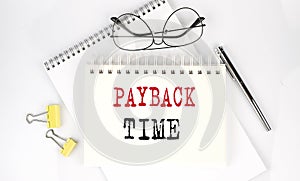 PAYBACK TIME text on the notebook with pen,clips and glasses