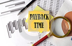 PAYBACK TIME text on a sticky on the graph background with pen and magnifier