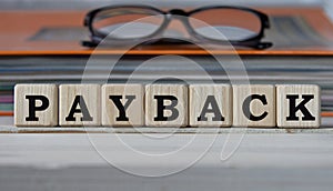 PAYBACK - word on wooden cubes on the background of a folder with documents and glasses