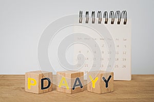 Payday loan concept. Flipped wooden cube block with yellow and grey pay day text and blurred white calendar on wood desk