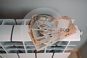 Paying bills. Hryvnia money banknotes on heating radiator battery at home. Expensive heating costs.