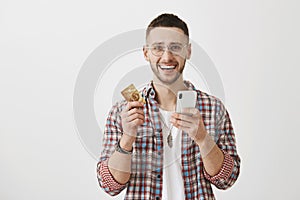 Paying bills with new app is ridiculously easy. Portrait of emotive and excited handsome man in glasses holding credit