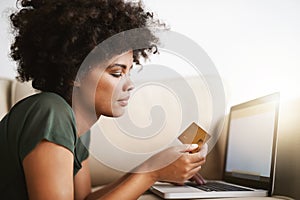 Paying the bills. a woman using her laptop on the sofa at home while holding a bankcard.