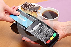 Paying with contactless credit card for cheesecake and coffee in cafe, finance concept