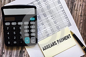 Payment arrears are written in a notepad, on a wooden table with a calculator and documents