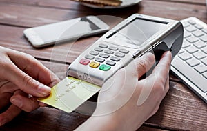 Payment by card in cafe with terminal and keyboard on wooden background