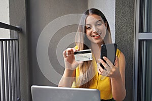 Payment with facial recognition. Attractive woman holding credit card and using smartphone at home. Businesswoman shopping online