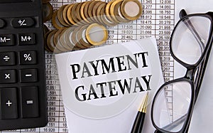 PAYMENT GATEWAY - words on a white piece of paper on the background of a calculator, pennies and glasses