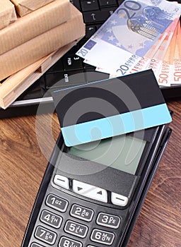Payment terminal with credit card, currencies euro, laptop and wrapped boxes on wooden pallet