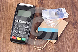 Payment terminal with credit card, currencies euro and paper shopping bag, concept of paying for shopping