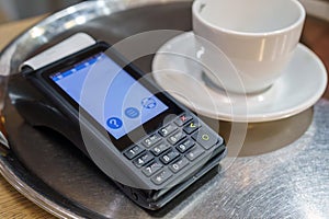 Payment terminal with nfc technology on a tray with a cup in a restaurant. Payment of breakfast with tpv