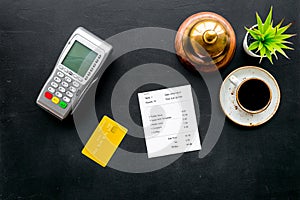 Payment terminal on restaurant desk near bill, service bell, coffee on black background top view