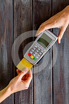 Payments in shops. Hand insert bank card in terminal on dark wooden background top-down copy space