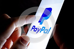 Paypal app icon on the smartphone screen and finger launching it