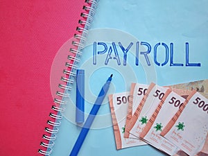 Payroll word on blue paper with money and pen