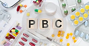 PBC - Primary biliary cholangitis, word on wooden blocks on a desk. Medical concept with pills, vitamins, stethoscope and syringe