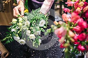 Pcture of white flowers in woman`s hands. She decorate them. Woman stands at black table. Red flowers are on picture as