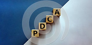 PDCA, plan do check act symbol. Wooden cubes with words `PDCA, plan do check act`. Beautiful white and blue background, copy spa