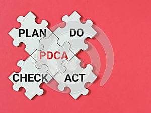 PDCA Plan Do Check Act written on jigsaw puzzle isolated on red background.