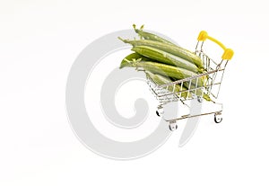 Pea pods in a mini shopping cart on a white background. Shopping, purchases, supermarket, mall concept. Copy space