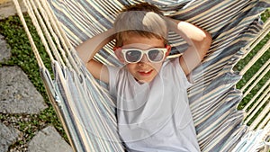 At peace in a garden a boy in sunglasses swings and lounges in a hammock, expressing the sensations of summertime, the