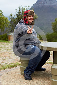 Peace out. An obese young man sitting outside at a picnic table showing a peace-sign.