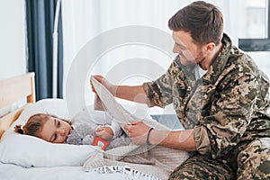 Peace and quiet. Soldier in uniform is at home with his little daughter