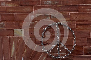 A peace symbol made of barbed wire and small figures in the shape of human bodies attached on a wall.