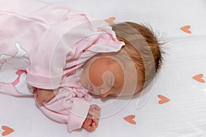 Peaceful baby lying on a bed with heart while sleeping in a bright room. The baby girl is 15 days old